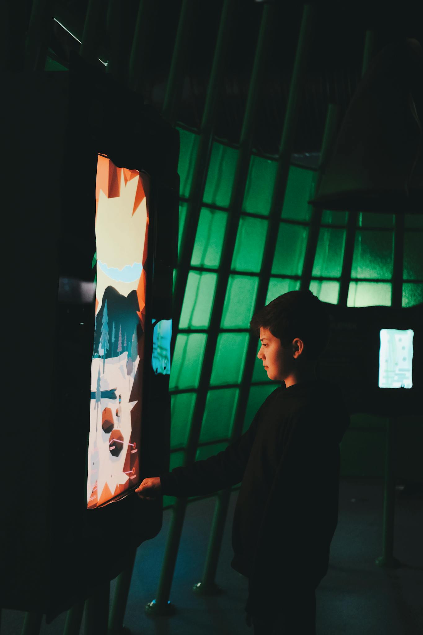 A young boy engages with a digital art installation in a dimly lit room.