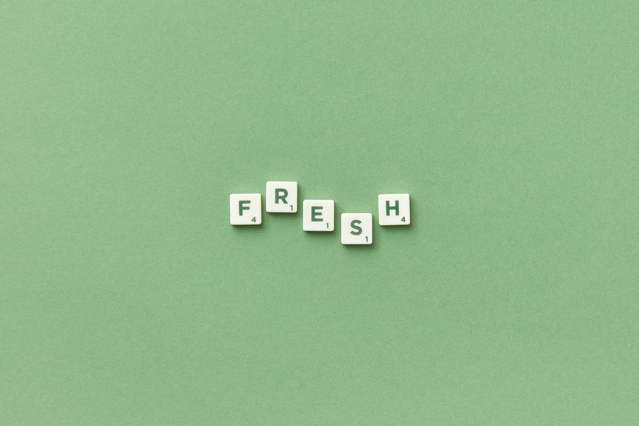 Scrabble tiles spelling 'FRESH' on a green background, perfect for word games or minimalist design themes.