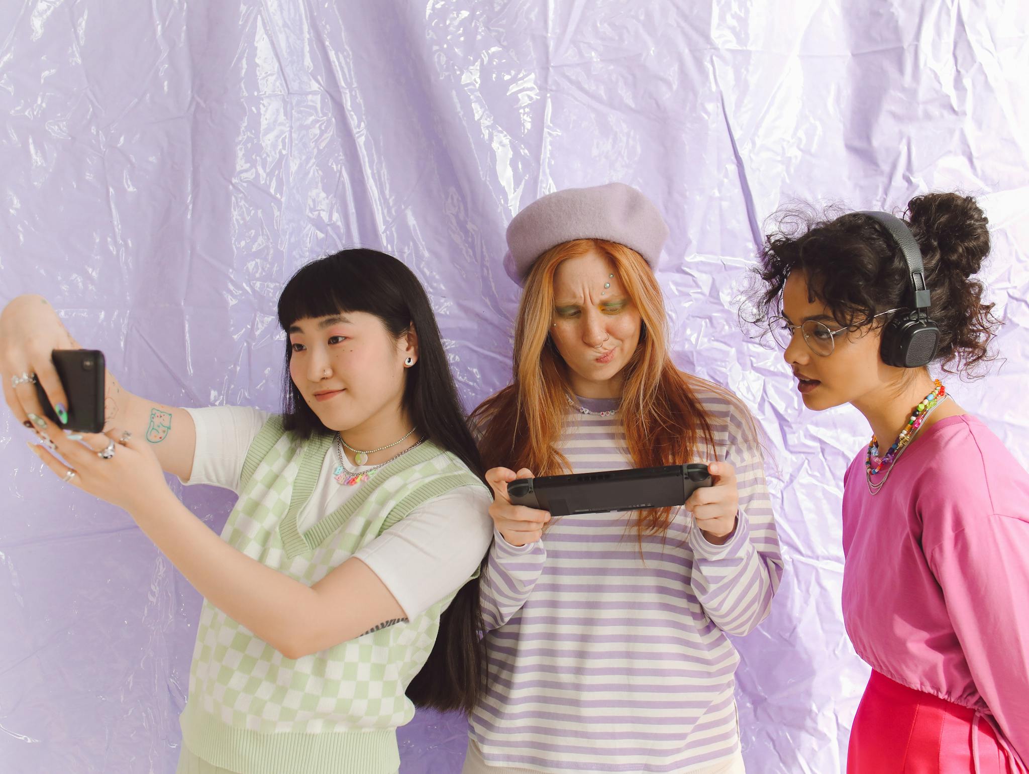 Three young women enjoying mobile gaming and selfies in a modern studio setting.